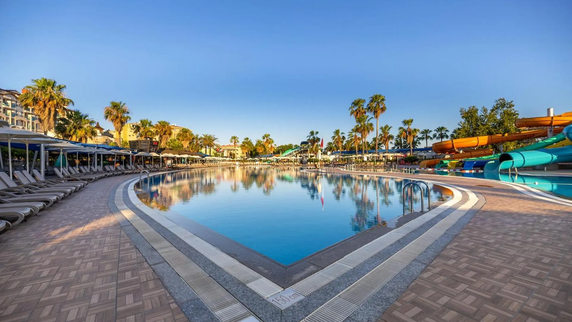 Vonresort Golden Coast & Aqua Side Exterior photo The photo captures a vibrant resort water park scene under a clear, bright blue sky. The foreground features a large, inviting swimming pool with crystal-clear turquoise water. The pool has a distinctive geometric design, with a wide, shallow area in
